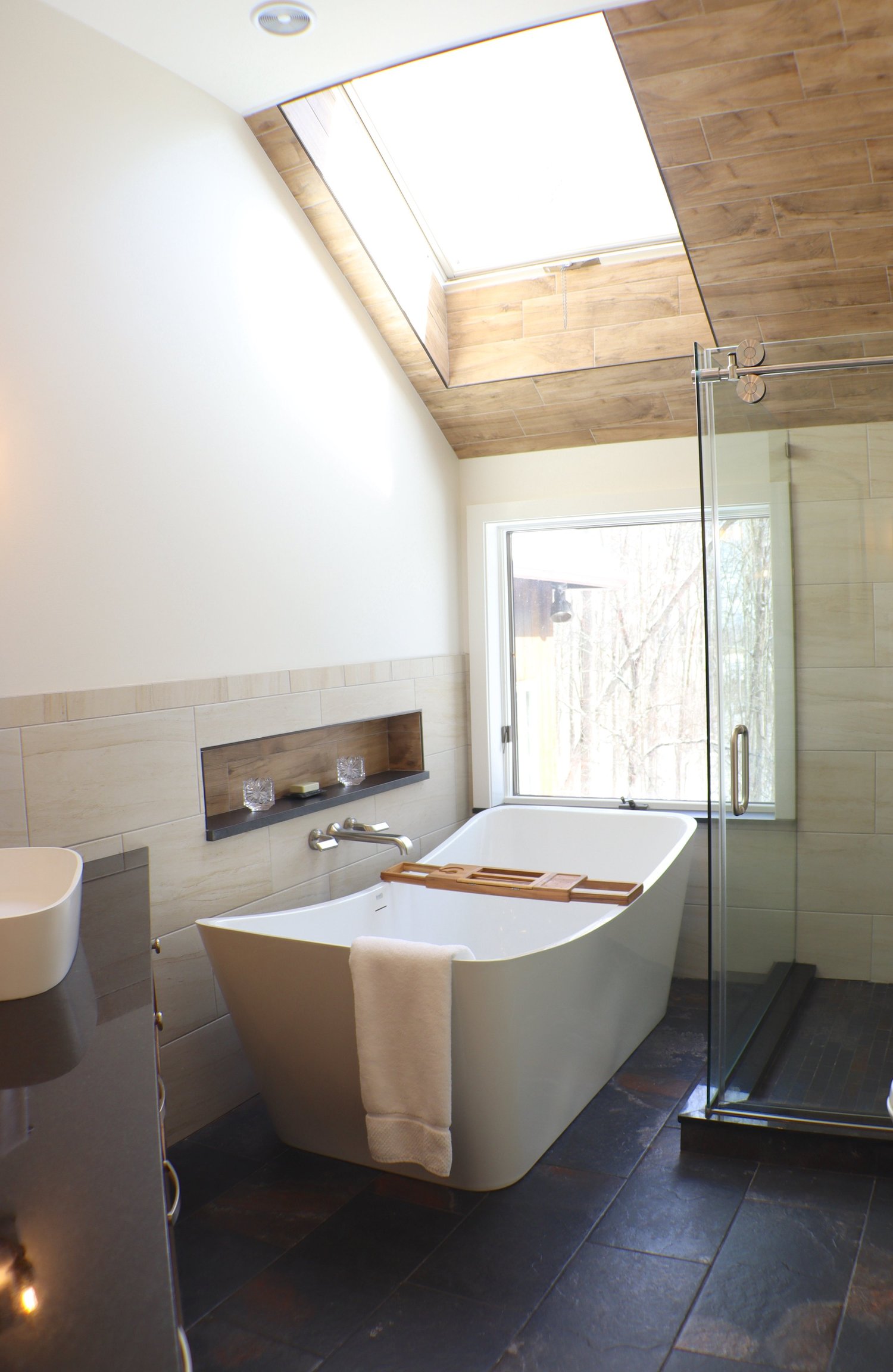 A spa-style bathroom remodel with a freestanding tub beneath a tall window and a tiled niche