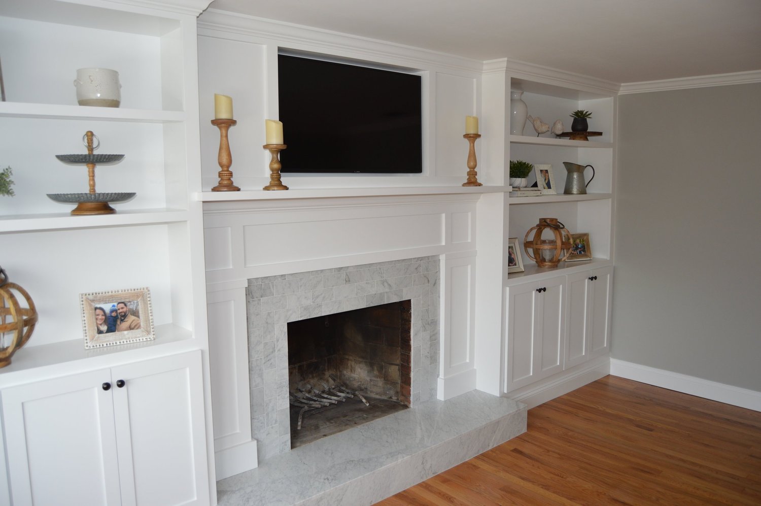 A living room with custom white built-in cabinetry flanking a marble fireplace surround