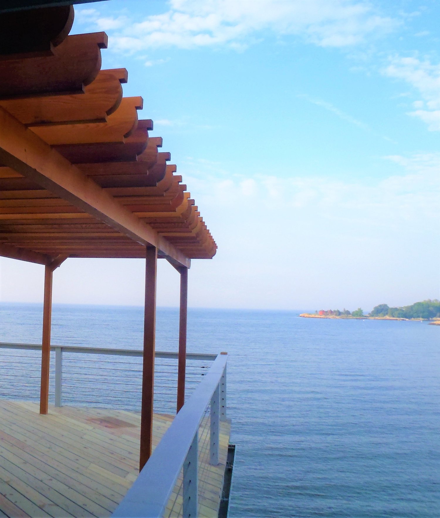A cedar pergola built over the water, framing a shoreline view at dusk