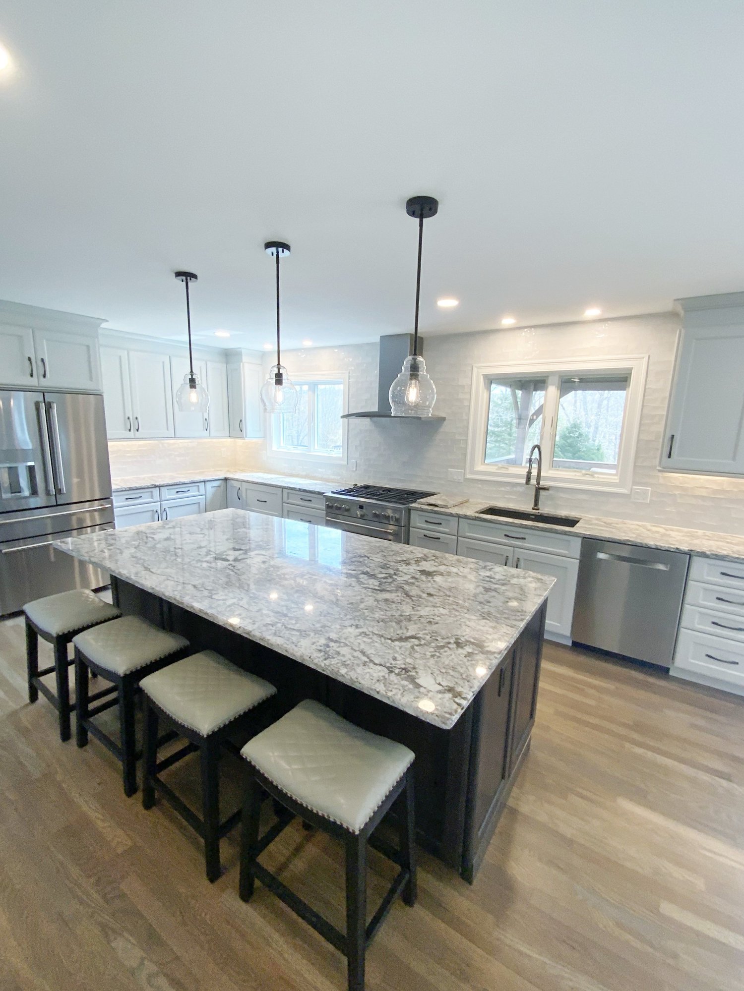 A bright white custom kitchen remodel with a large granite island and pendant lighting, built by TRP Construction