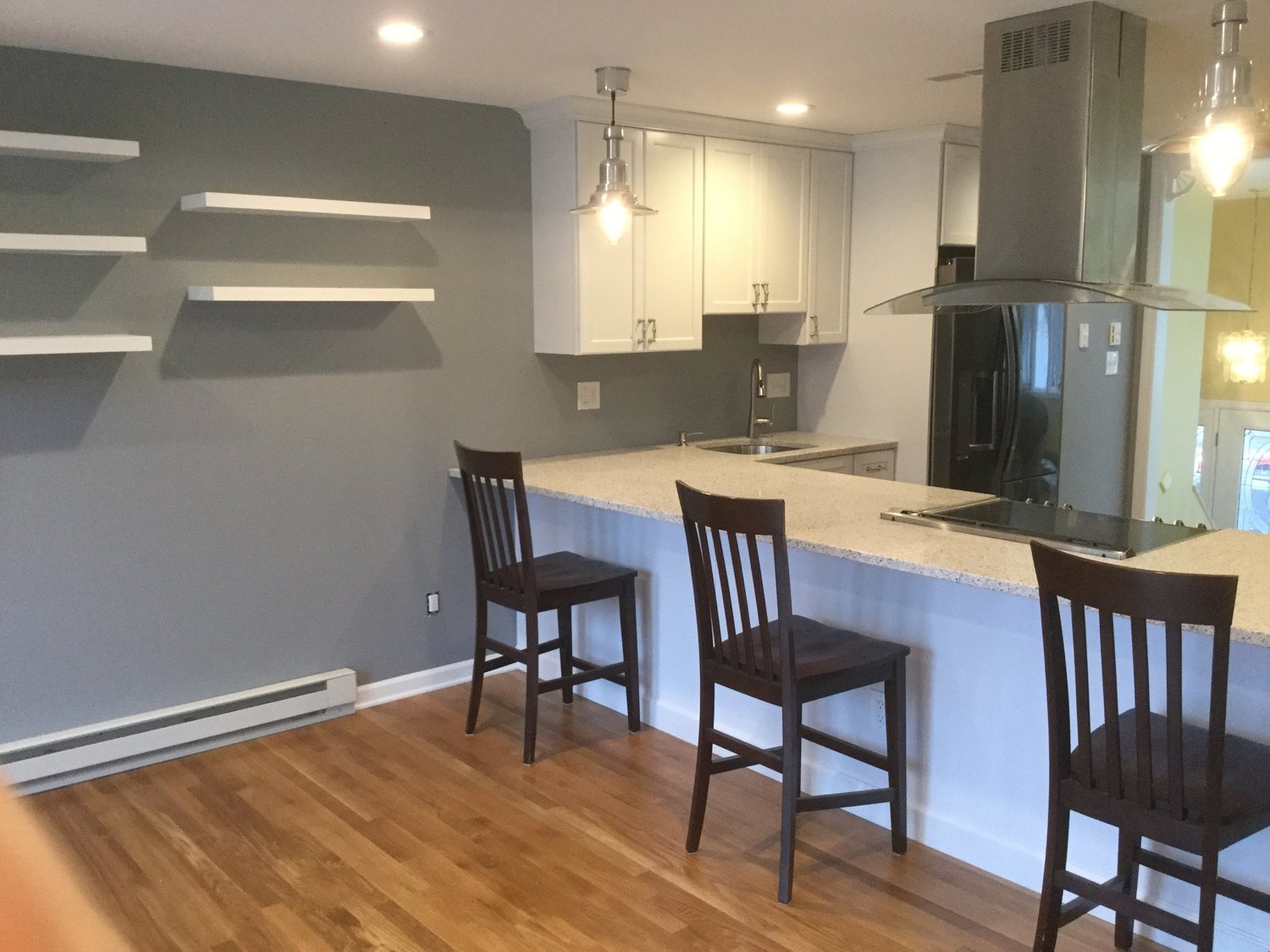A white custom kitchen with a granite island, counter stools, and floating shelves